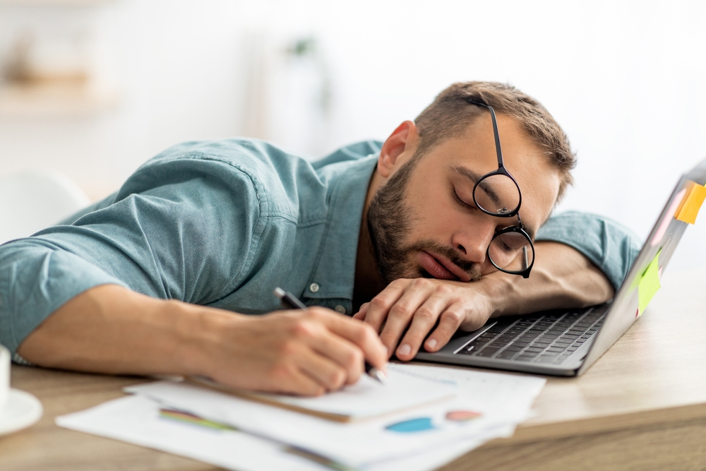 Exhausted,Millennial,Man,Sleeping,On,His,Office,Desk,,Next,To man falling asleep at work