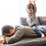 Tired young father carrying a boy on his back, depicting the physical demands of parenting and resulting sleep deprivation