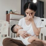 Tired Asian mother experiencing sleep deprivation and exhaustion while caring for her child at home