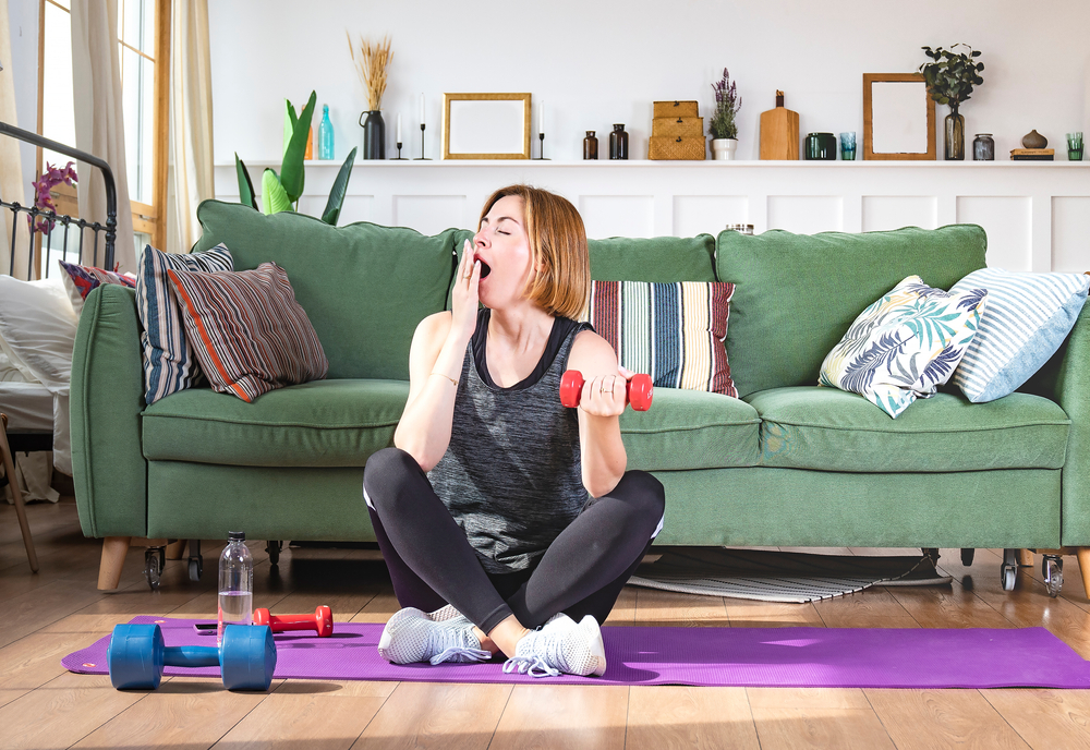 Woman stretching on a fitness mat while yawning, illustrating fatigue from athletic activity and the need for sleep recovery